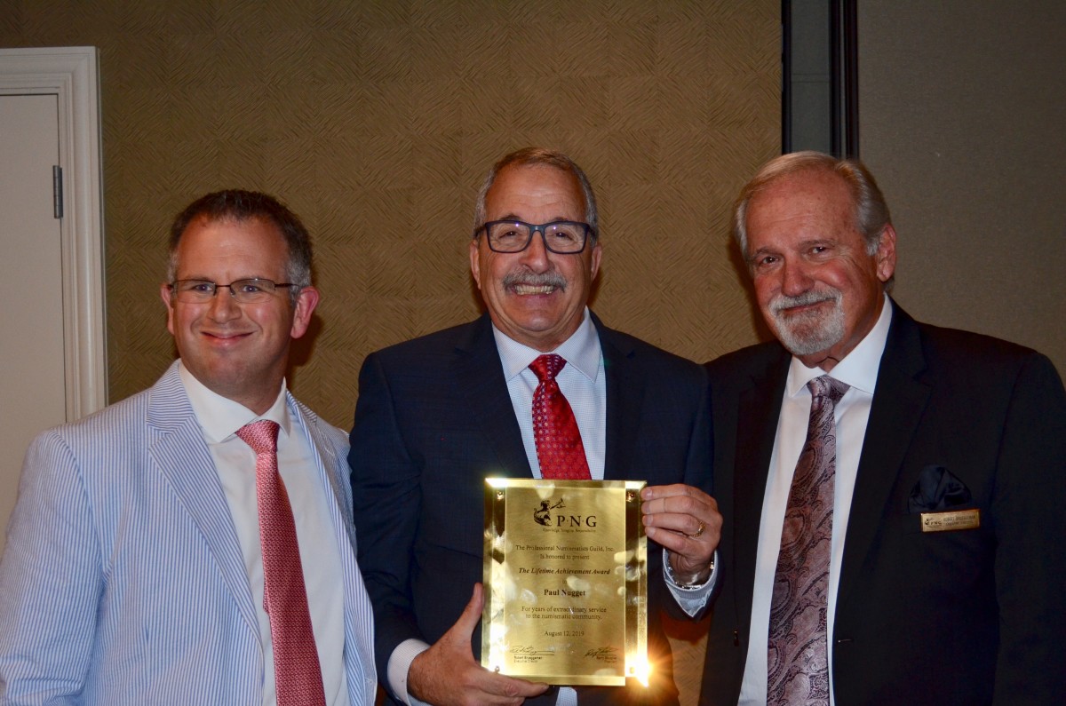 Paul Nugget (center) was presented the PNG 2019 Abe Kosoff Founders Award by PNG member-dealer John Brush (left) and PNG Executive Director Robert Brueggeman (right). (Photo credit: Donn Pearlman.)