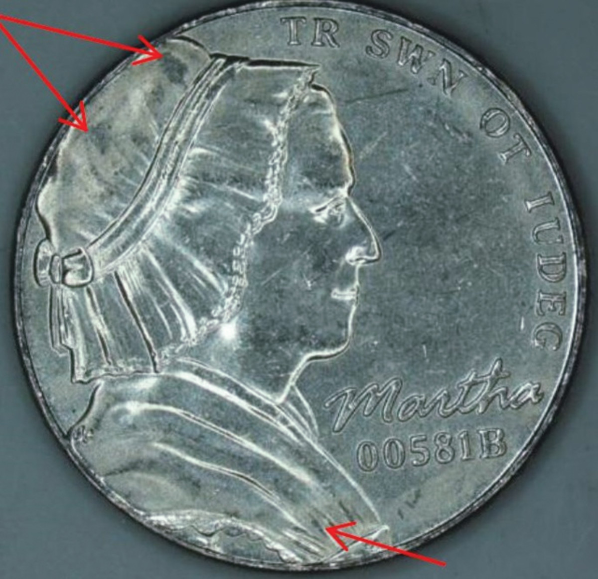 Martha Washington’s portrait was used on test strikes of various compositions for the nickel. This one is multi-ply plated steel. The arrows indicate areas where planchet metal did not flow completely into the recesses of the die when struck under 54 tonnes to 60 tonnes pressure. Regular nickels are struck with 54 tonnes pressure.