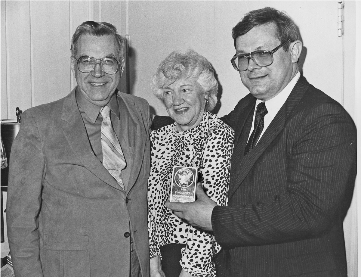 Friendly competitors Chet Krause (left) and Clifford Mishler give a silver round to longtime Coin World editor Margo Russell.